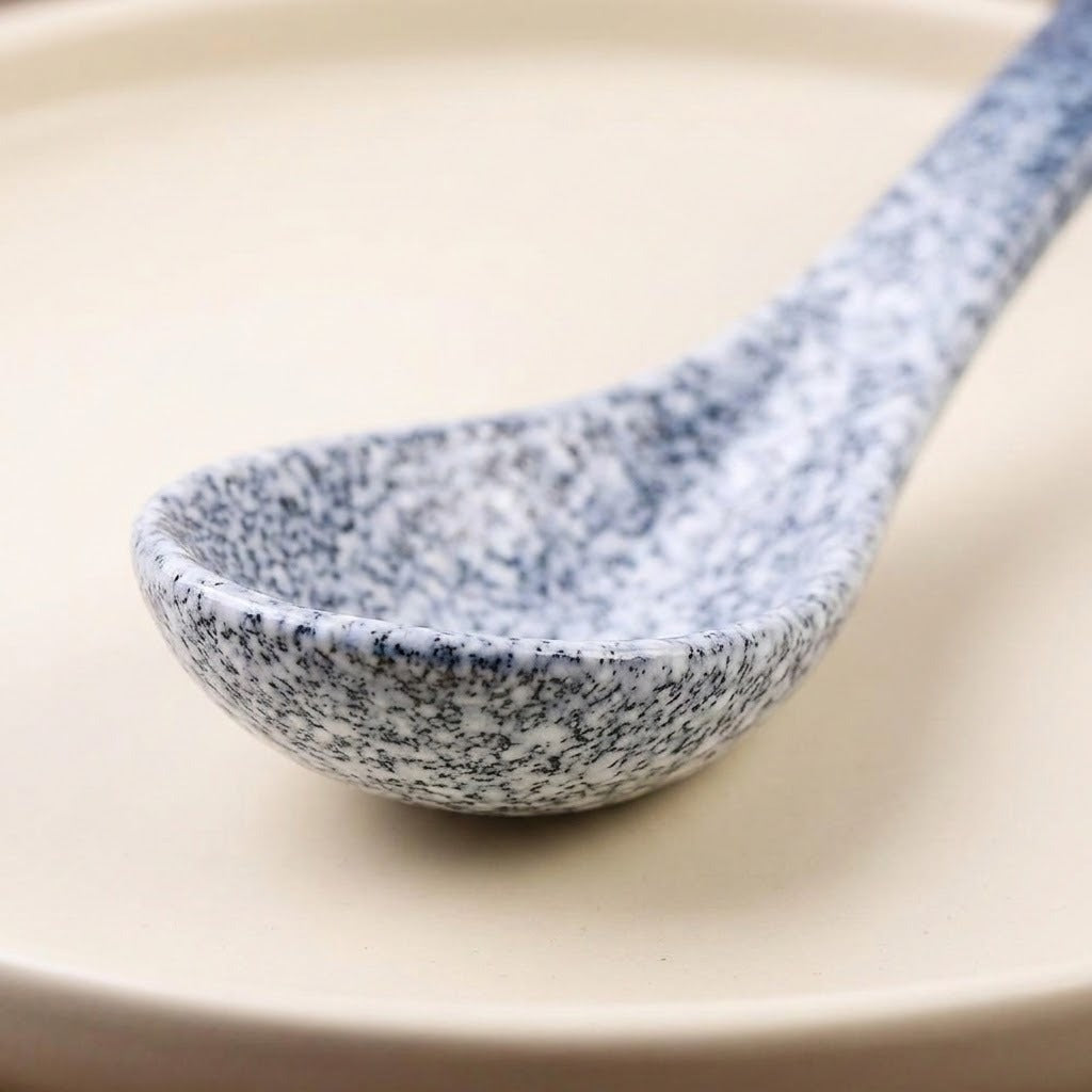 A close-up of a speckled ceramic spoon with a blue and white marbled pattern, resting on a warm beige plate.