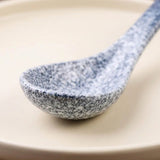 A close-up of a speckled ceramic spoon with a blue and white marbled pattern, resting on a warm beige plate.