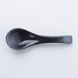 A single dark ceramic spoon with a textured, speckled black and gray glaze, photographed on a clean white background.