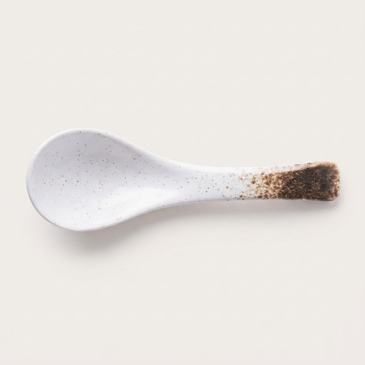 A white ceramic spoon with fine brown speckles and a dark brown speckled handle, shown on a light beige background.
