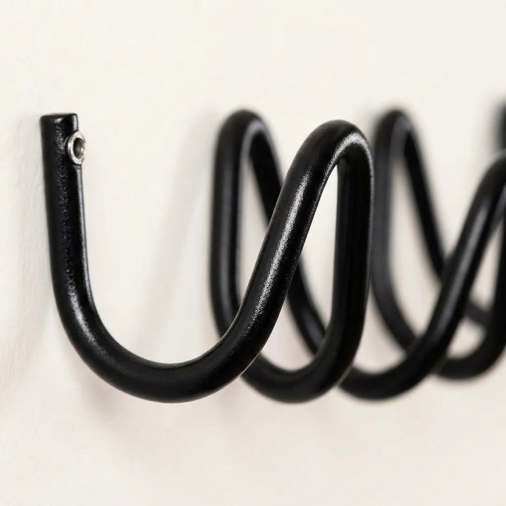 A close-up of a black metal spiral wall hook mounted on a plain off-white wall.