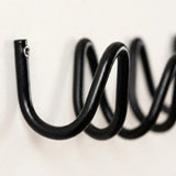 A close-up of a black metal spiral wall hook mounted on a plain off-white wall.