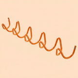 An orange spiral-shaped wall hook mounted on a solid pale peach background.