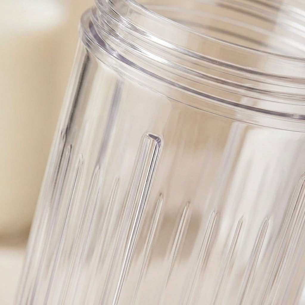 Close-up of a clear ribbed plastic blender jar cup with a threaded opening, shown against a softly blurred warm beige background.