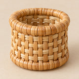 Natural tan basket-weave rattan napkin ring centered on a warm beige studio backdrop.