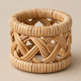 Natural tan open-weave braided rattan napkin ring centered on a soft tan studio backdrop.