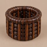 Dark brown basket-weave rattan napkin ring centered on a muted cocoa studio backdrop.