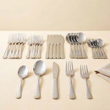 A set of polished stainless steel cutlery, including forks, spoons, and knives, neatly arranged on a light beige surface against a matching beige background.