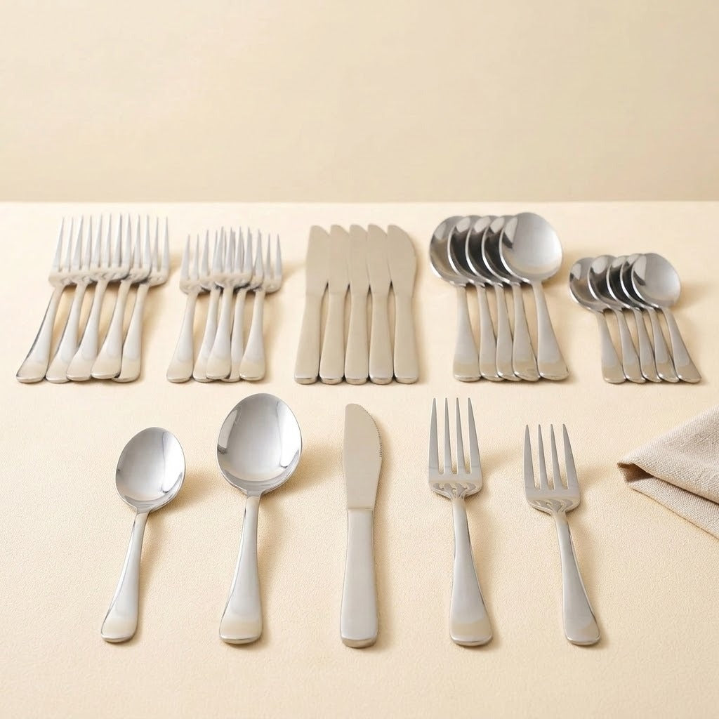 A set of polished stainless steel cutlery, including forks, spoons, and knives, neatly arranged on a light beige surface against a matching beige background.