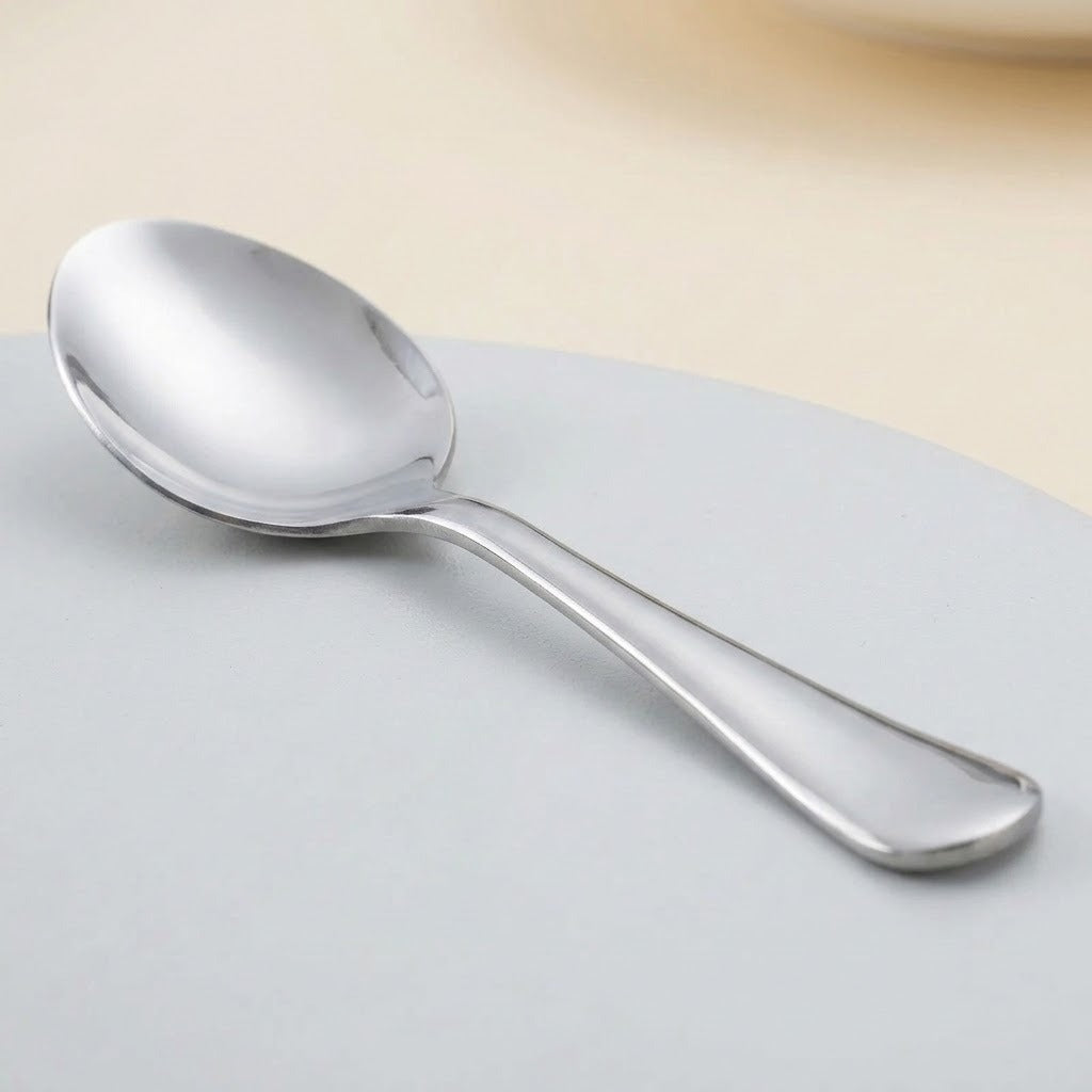 A polished stainless steel spoon resting on a light gray surface with a soft beige background.