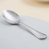 A polished stainless steel spoon resting on a light gray surface with a soft beige background.