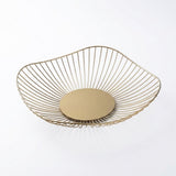 A modern wire bowl with a gold finish, featuring a slatted open design and a solid circular base, shown on a clean white background.