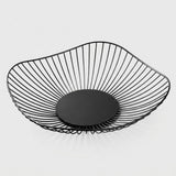 A modern black wire bowl with a slatted open design and a solid circular base, shown on a light gray background.