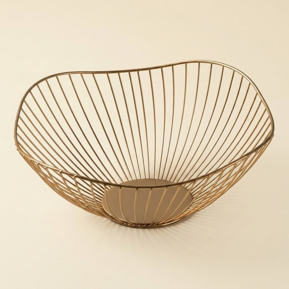A modern wire bowl with a slatted design in a warm metallic gold finish, set against a solid cream background.