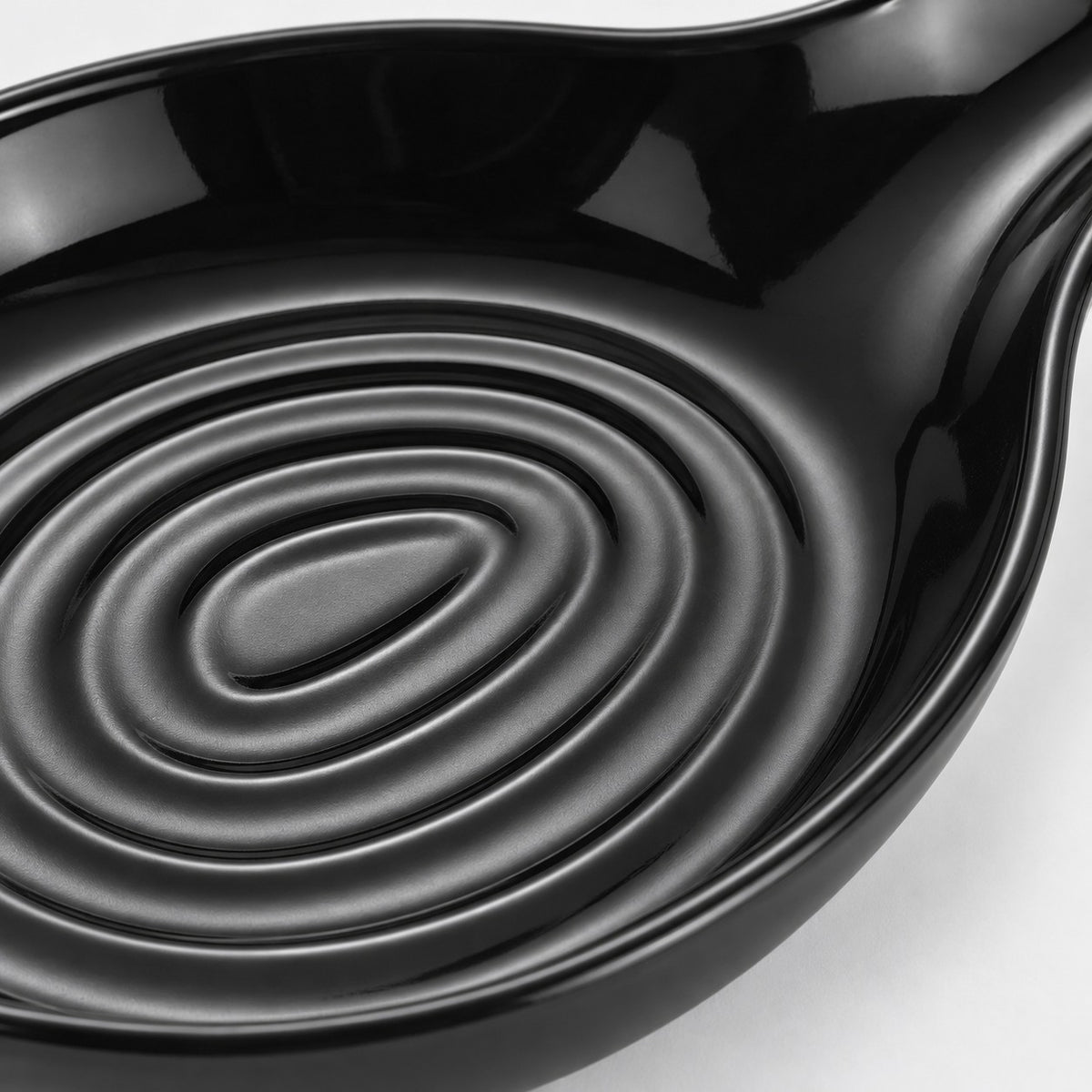 Macro view shows the spoon rest’s glossy black plastic finish and raised oval bowl grooves.
