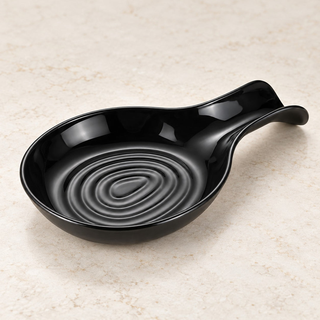 Glossy black plastic spoon rest has a grooved oval bowl and curved integrated handle.