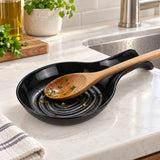 A black spoon rest holds a rinsed cooking spoon beside a bright kitchen sink.