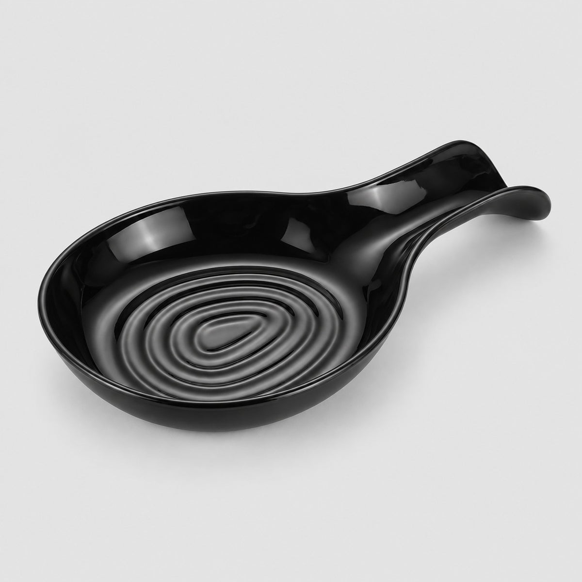 Black plastic spoon rest with a grooved bowl on a pale gray studio backdrop.