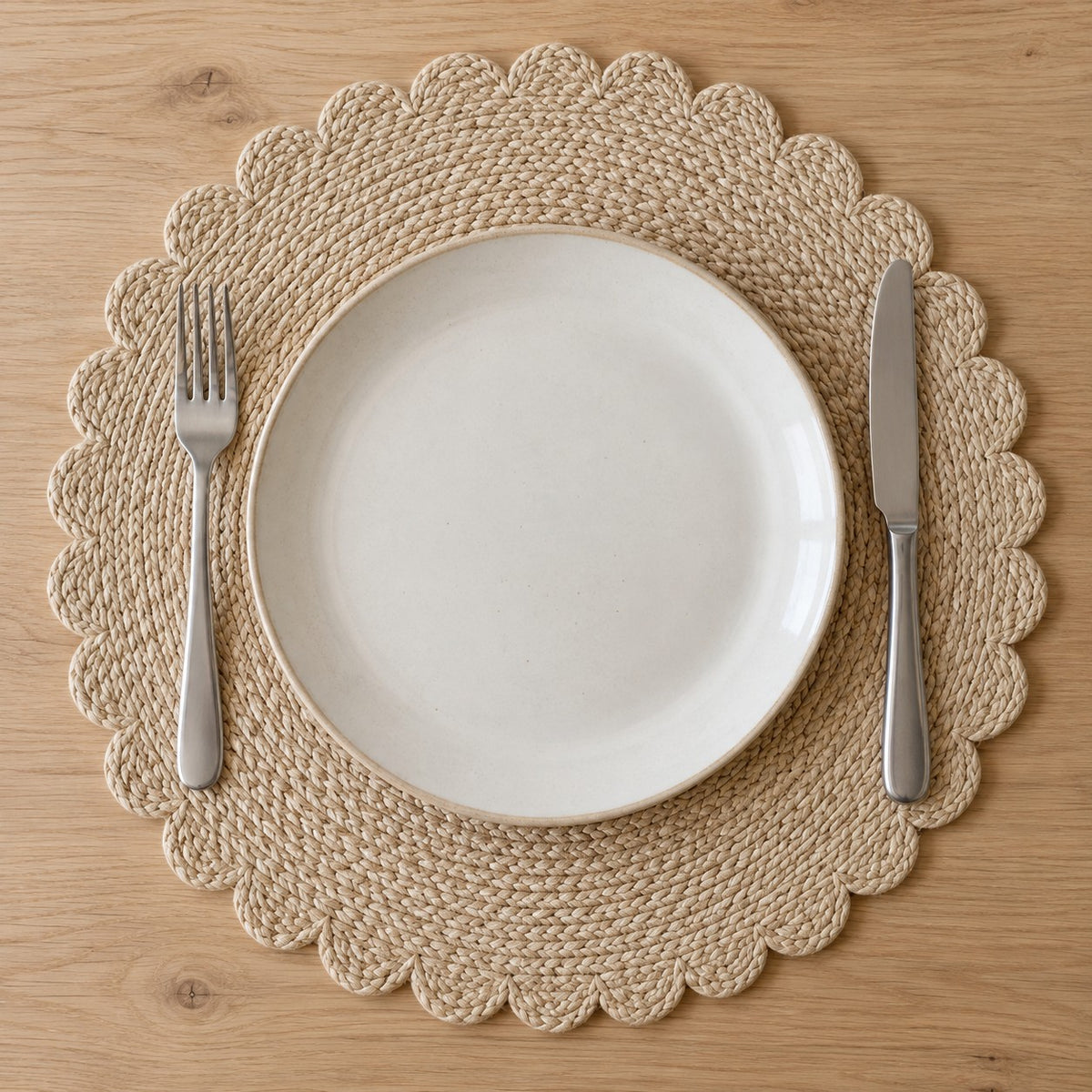 Beige round woven placemat shown with a dinner plate, fork and knife for scale.