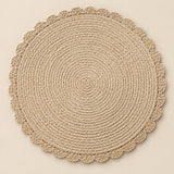 Single beige round woven placemat with braided edge on a pale beige backdrop.