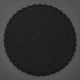 Single black round woven placemat with braided edge on a light gray backdrop.