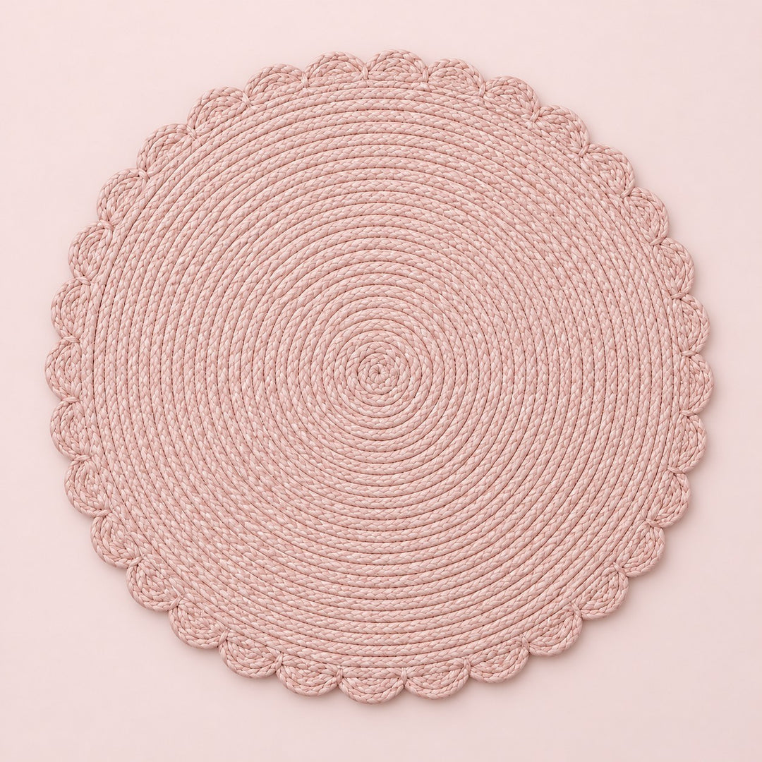 Single pink round woven placemat with braided edge on a pale blush backdrop.