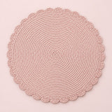 Single pink round woven placemat with braided edge on a pale blush backdrop.
