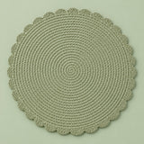 Single green round woven placemat with braided edge on a light sage backdrop.