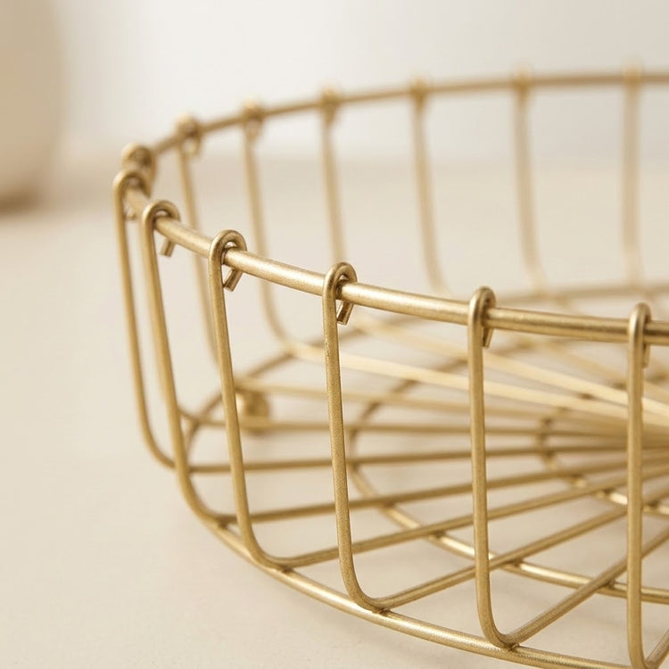Close-up of a gold metal wire basket tray on a light beige surface with a soft blurred background.
