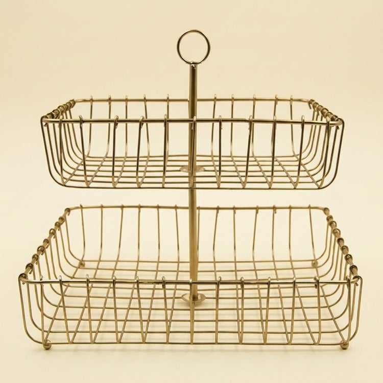 A two-tier wire basket serving tray with a central handle, finished in a warm gold or brass tone, set against a solid cream background.