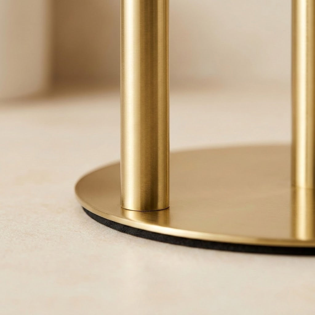 Close-up of a round gold metal base with two vertical gold cylindrical legs on a light beige surface.