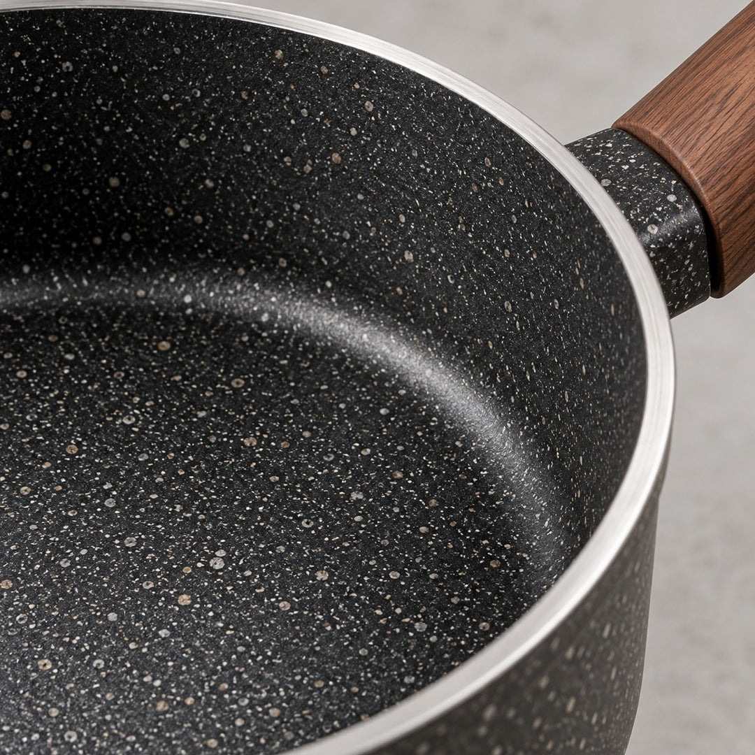 Close detail of the saucepan's speckled nonstick surface, silver rim, and wooden handle fitting.