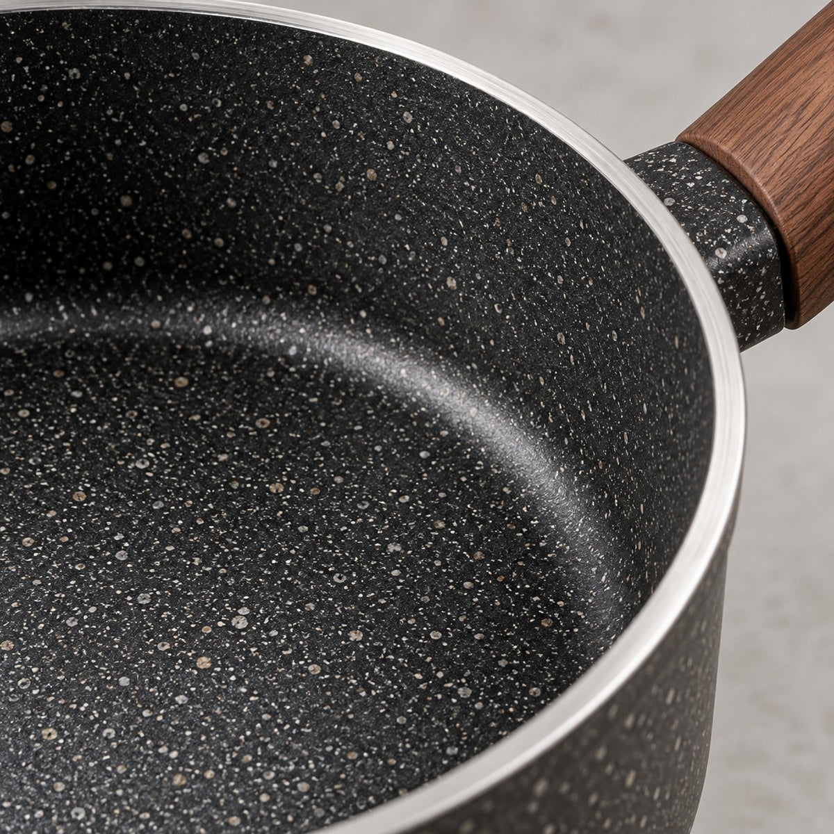 Close detail of the saucepan's speckled nonstick surface, silver rim, and wooden handle fitting.