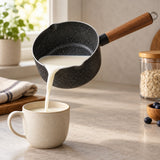 Nonstick saucepan with pour spout sends warm milk neatly into a cup on a kitchen counter.