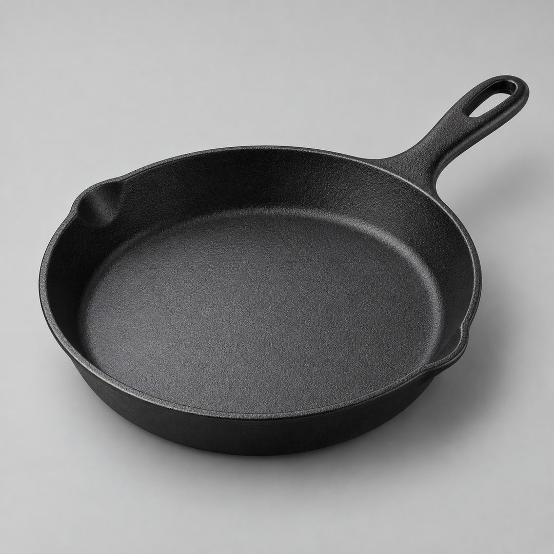 Round black frying pan with integrated handle and smooth interior on a pale studio backdrop.