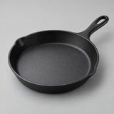 Round black frying pan with integrated handle and smooth interior on a pale studio backdrop.