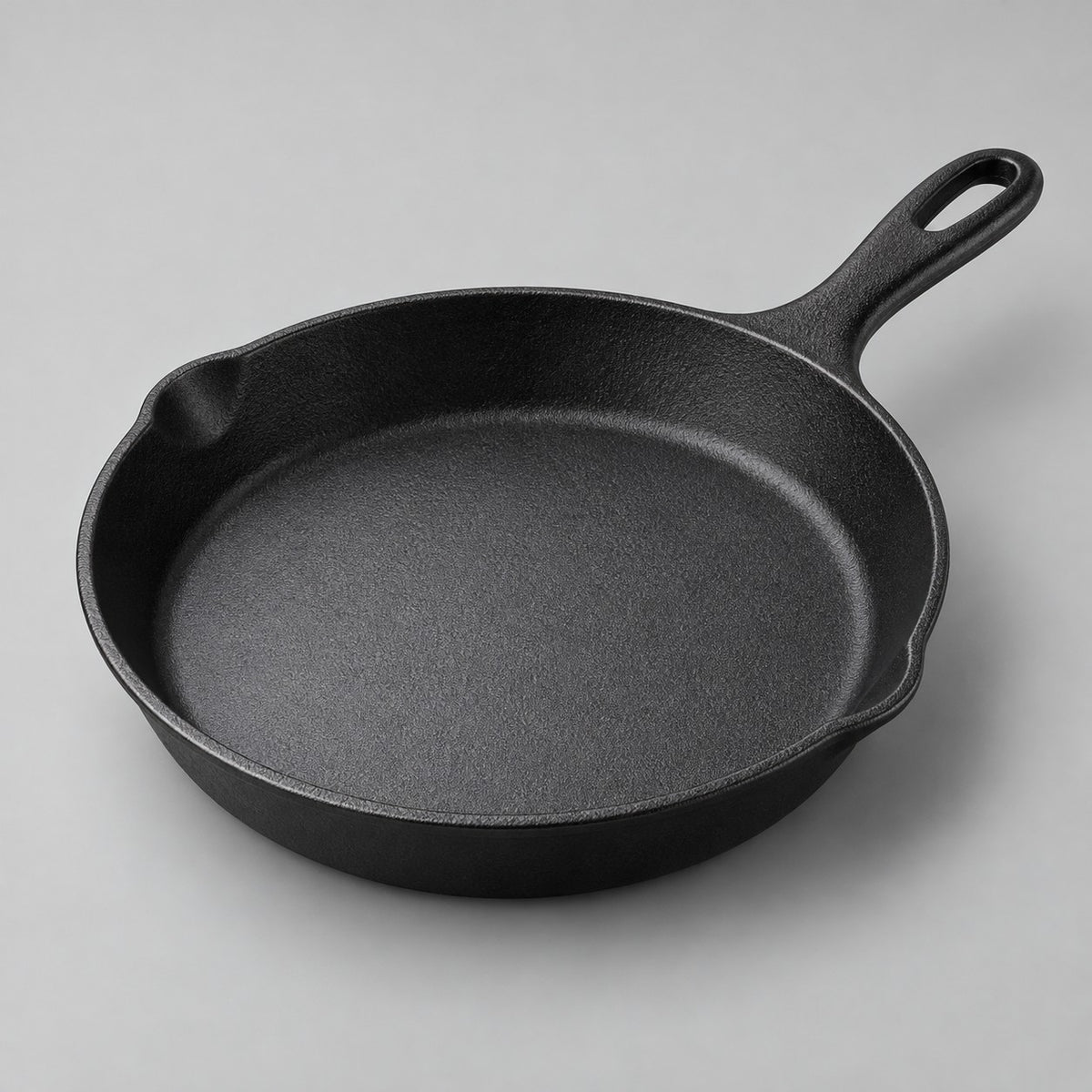 Round black frying pan with integrated handle and smooth interior on a pale studio backdrop.
