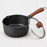 Speckled saucepan with wooden handle and clear glass lid with brown knob on a pale backdrop.