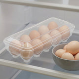 A clear plastic egg carton holding several eggs, placed on a refrigerator shelf next to a gray bowl of eggs.