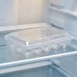 A clear plastic refrigerator egg tray with a matching lid, shown on a glass shelf inside an open refrigerator.