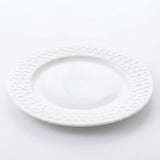 A white ceramic plate with a textured, dimpled pattern around the rim, shown on a clean white background.