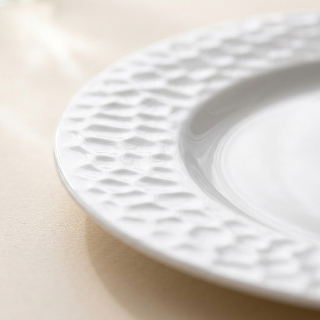 A close-up of a white ceramic plate with a textured, dimpled border, resting on a light beige surface.