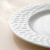 A close-up of a white ceramic plate with a textured, dimpled border, resting on a light beige surface.