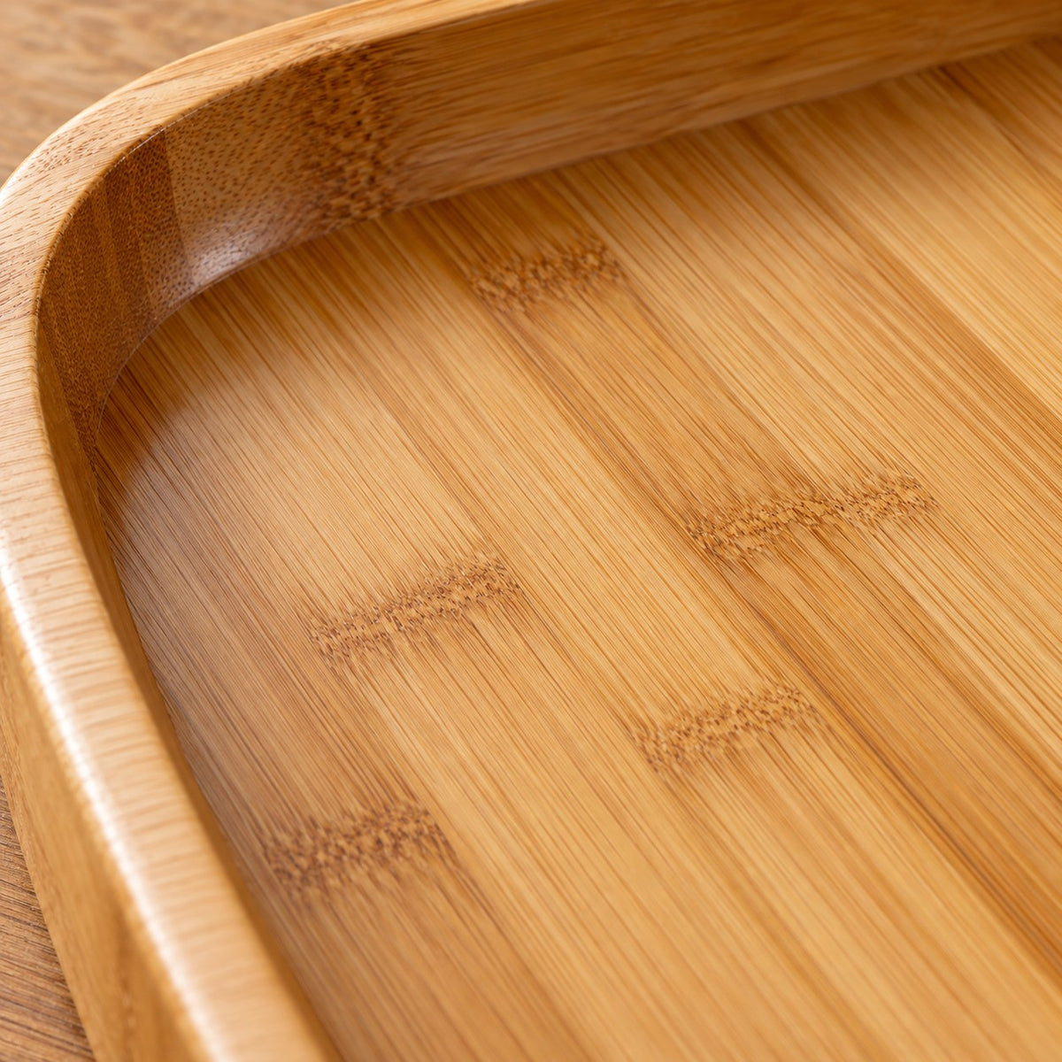 Close-up of the bamboo and wood serving tray's polished honey-colored grain and smooth inner rim.