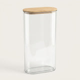 A tall, clear glass canister with a rounded rectangular base and a light natural wood lid, shown on a clean off-white background.