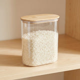 A clear rectangular plastic storage jar filled with white rice, featuring a light natural wood lid, sitting on a light wood shelf.