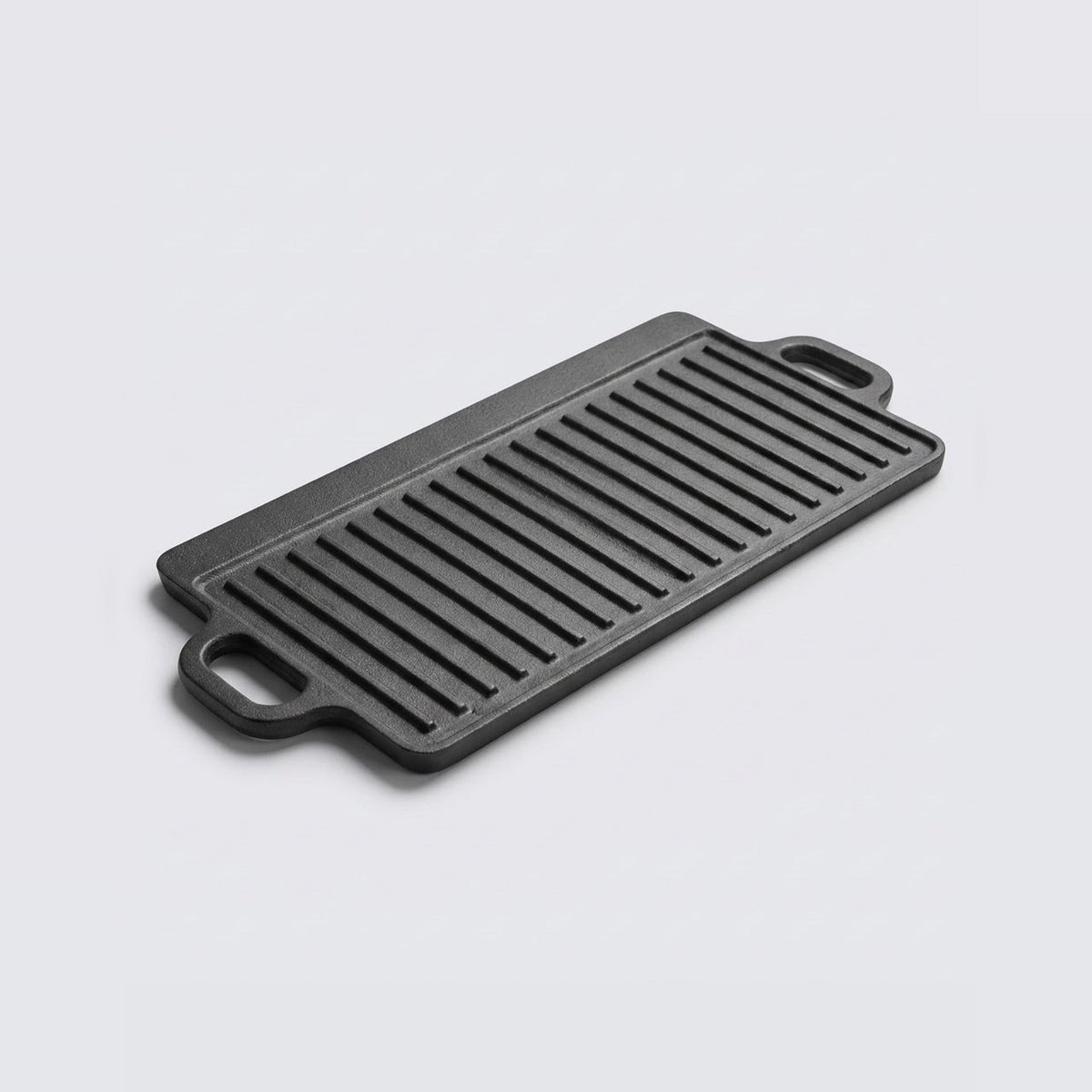A rectangular black cast iron griddle plate with two loop handles, shown at an angle on a light gray background.