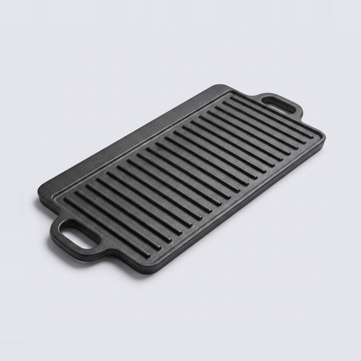 A rectangular black cast iron griddle plate with two side handles, shown at an angle on a light gray background.