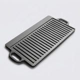 A rectangular black cast iron griddle plate with two handles and parallel ridges, photographed on a light gray background.