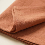 A close-up of folded terracotta-colored textured fabric, showing its woven linen-like pattern against a light neutral background.